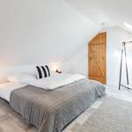 Bedroom with bed, clothing rack, and wooden door under sloped ceiling.