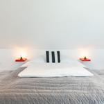 Bedroom with double bed, gray quilt, and two red nightstands with lamps.