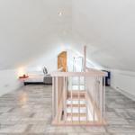 Attic room with bed, wooden railing, and wooden floor.