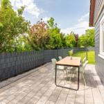 Terrace with table and chairs, surrounded by greenery and a black fence.
