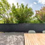 Backyard with table, chairs, and flowers. Black wall, trees, and flowers.