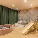 Kinderzimmer mit Ballpool, Giraffenrutsche und Sofa an der Steinwand.