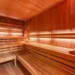 Holzsauna mit mehreren Sitzreihen und einem Eimer mit Schöpflöffel.