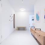 Hallenflur mit Holzschrank, Wandkunst und Sitzbank. Weiße Wände und Boden.