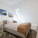 Schlafzimmer mit Dachschräge, Bett, Sessel und Wandbildern.