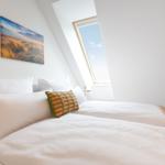 Schlafzimmer mit Dachfenster, Bett mit Kissen und Wandbildern.