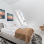 Schlafzimmer mit Dachschrägen, Bett, Sessel und Fenster. Zwei Bilder an der Wand.