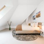 Schlafzimmer mit Dachschrägen, Bett, Teppich und Wandbildern.