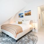 Schlafzimmer mit Dachschräge, Bett, Teppich und Wandbildern. Tür führt in Flur.