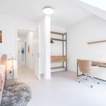 Schlafzimmer mit Bett, Schreibtisch und Kleiderschrank. Wandbild und Stehlampe sichtbar.