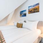 Schlafzimmer mit Bett, Kissen und Wandbildern an schräger Wand.