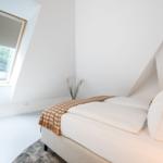 Schlafzimmer mit Dachschräge, Bett und Dachfenster mit Blick auf Grün.