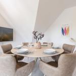 Rundes Esszimmer mit sechs Stühlen, Tischdekoration und Wandbild.