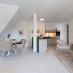 Wohn- und Essbereich mit Küche unter Dachschrägen. Moderne Einrichtung mit Sofa, Stühlen und Tisch.
