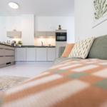 Ein Wohnbereich mit Sofa, Küchenzeile und Wandbild.