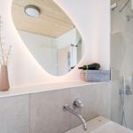 Badezimmer mit Waschbecken, Dusche und beleuchtetem Spiegel.