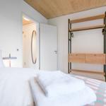 Schlafzimmer mit Bett, Kleiderständer und Tür zum Badezimmer.
