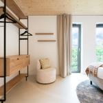 Schlafzimmer mit Bett, Kleiderschrank und Sitzgelegenheit. Fenster mit Blick auf Grün.