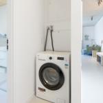 Waschmaschine im Flur neben Bad und Wohnbereich.