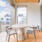 Terrasse mit runden Tisch und Stühlen, Holzboden und Blick auf Wohngebäude.
