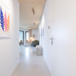 Flur mit weißen Wänden, Holzdecke und Kunstwerk an der Wand. Blick in das Wohnzimmer.