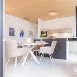 Essbereich mit Tisch und Stühlen, Kücheninsel und TV. Holzdecke und weiße Wände.