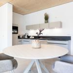 Rundtisch mit Stühlen vor moderner Küche mit Holzdecke und Wandbild.