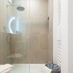 Dusche mit Glaswand, beleuchtetem Spiegel und Handbrause.