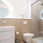 Badezimmer mit Dusche, Waschbecken und Toilette. Moderne Einrichtung mit beleuchtetem Spiegel.
