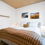 Schlafzimmer mit Bett, Wandbildern und Holzdecke.