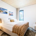 Doppelbett mit Kissen und Decke, Sessel, Lampe und Wandbilder
