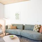 Ein Wohnzimmer mit einem grauen Sofa, einem weißen Sessel und einer runden Tischplatte.