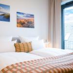 Doppelbett mit Kissen und Decke, Wandbilder und Fenster mit Balkonansicht.
