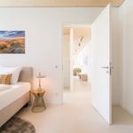 Schlafzimmer mit Bett, Nachttisch und Blick in Flur. Wandbild und Holzdecke sichtbar.