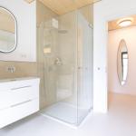 Badezimmer mit Dusche, Waschbecken und Spiegel. Holzdecke und helle Wände.