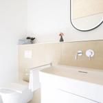 Badezimmer mit Waschbecken, Spiegel und Toilette. Helle Wände und moderne Armaturen.