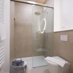 Badezimmer mit Dusche, Toilette und Waschbecken. Glaswand, Holzdecke und beige Fliesen.