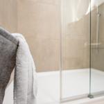 Dusche mit Glaswand und weiße Badewanne mit Handtuch.