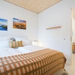 Schlafzimmer mit Bett, Wandbildern und Holzdecke. Tür führt in angrenzenden Raum.