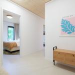 Flur mit Holzschrank und Wandbild. Durchgang zu Schlafzimmer mit Bett und Fenster.