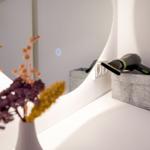 Spiegel mit Touch-Display, Haartrockner und Trockenblumen auf einem weißen Schrank.