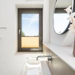 Badezimmer mit Waschbecken, Spiegel und Fenster mit Jalousie.