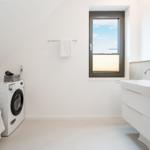 Badezimmer mit Waschmaschine, Waschtisch und Fenster.