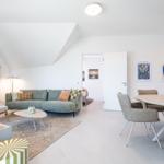 Wohn- und Essbereich mit Sofa, Tisch und Stühlen. Dachschräge und Wandbilder sichtbar.