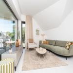 Ein Wohnzimmer mit grünem Sofa, Holztisch und großem Fenster zur Terrasse.