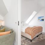 Schlafzimmer mit Dachschräge und großem Fenster. Wohnbereich mit Sofa und Kissen.