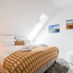 Schlafzimmer mit Dachfenster, Bett, Sessel und Wandbildern.