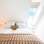 Schlafzimmer mit Dachfenster, Bett mit Kissen und Decke, zwei Nachttische mit Lampen.