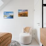 Schlafzimmer mit Dachschräge, Bett, Sessel und Wandbildern.