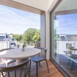 Terrasse mit runden Tisch und Stühlen. Blick auf Wohnhäuser und Bäume.